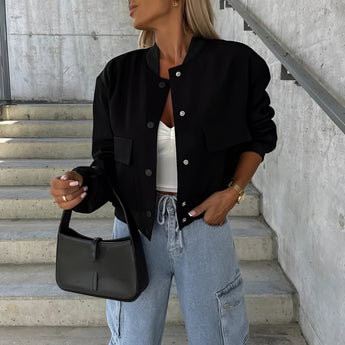 
A woman wearing a black cropped puffer jacket styled as casual fashion outerwear, paired with jeans. She is standing and wearing sunglasses, giving a stylish and modern look.