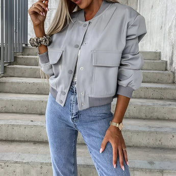 Women's gray cropped puffer jacket, styled casually with denim jeans. The outerwear features a high neck and is designed for a fashionable look, highlighting the shoulder and arm fit.