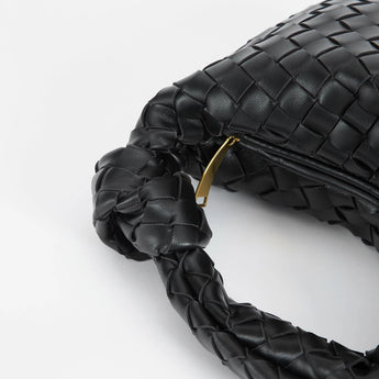 Black leather geometric woven handbag with designer braided details displayed against a monochromatic background.