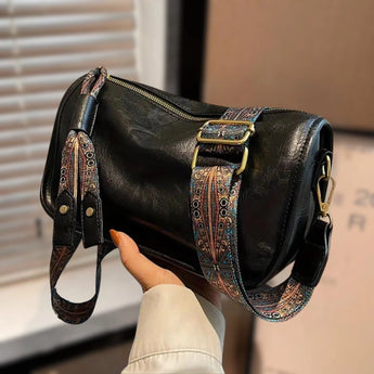 A black boho leather handbag with artisan embroidery, styled as a crossbody bag, is worn by a person dressed in casual attire including jeans and a long-sleeved top, accessorized with sunglasses.