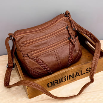 Brown braided leather crossbody bag for women with multiple zippers, featuring a shoulder strap and a sleek, stylish design.