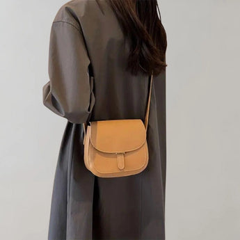 Brown leather crossbody saddle bag for women, featuring a minimalist design, displayed with a strap over the shoulder.