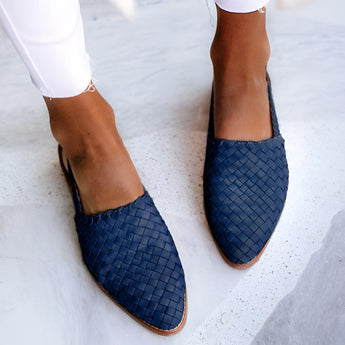 Women's stylish slip-on brown woven leather loafers paired with a blue variant, featuring a detailed view of the footwear on a model's leg and foot against a white background.