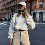 A woman wearing a trendy cozy Sherpa fleece cropped jacket, styled for winter outerwear, with a focus on the plush texture and tailored fit, standing in a room near a window. She has a casual hairstyle and accessorizes with eyewear, highlighting the jacket's sleeve and shoulder details.