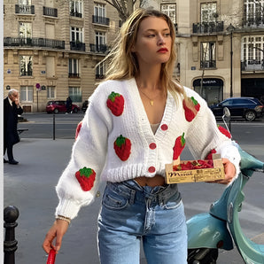 Red strawberry knit cardigan styled with blue jeans, featuring a trendy V-neck design, displayed on a mannequin near a large window.