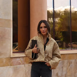 Textured gold metallic bomber jacket for women featuring long sleeves and a chic design, modeled by a person standing against a brick background.