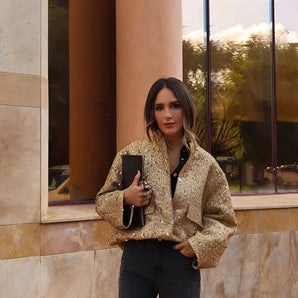 Textured gold metallic bomber jacket for women featuring long sleeves and a chic design, modeled by a person standing against a brick background.