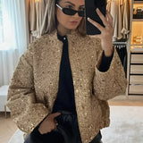 
Woman wearing a textured gold metallic bomber jacket, styled with black sunglasses and fashionable accessories.