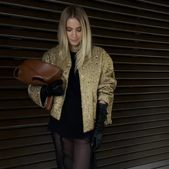 Textured gold metallic bomber jacket worn by a woman, featuring a shiny finish, long sleeves, and a ribbed collar, standing in a pose that highlights the waist and thigh area. 