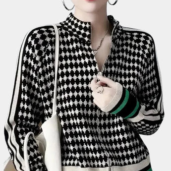 
A close-up image of a women's houndstooth turtleneck sweater in a black and white pattern, featuring a visible hand and arm, highlighting the texture and design of the knitwear.