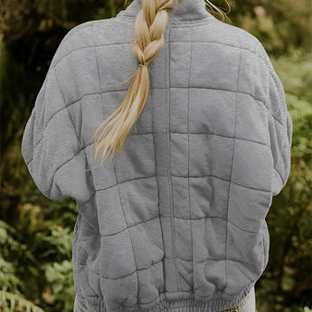 Women's lightweight insulated forest green quilted jacket displayed outdoors on grass, showing the jacket's design with long sleeves and quilted texture for warmth and style.