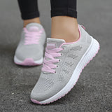 Women's lightweight gray-pink sneakers designed for running, featuring breathable materials. The shoes are shown worn on feet, highlighting their stylish and sporty appearance.